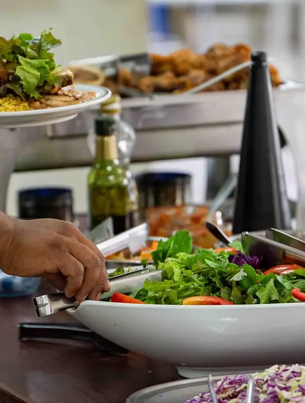 Mão servindo salada fresca no bufê