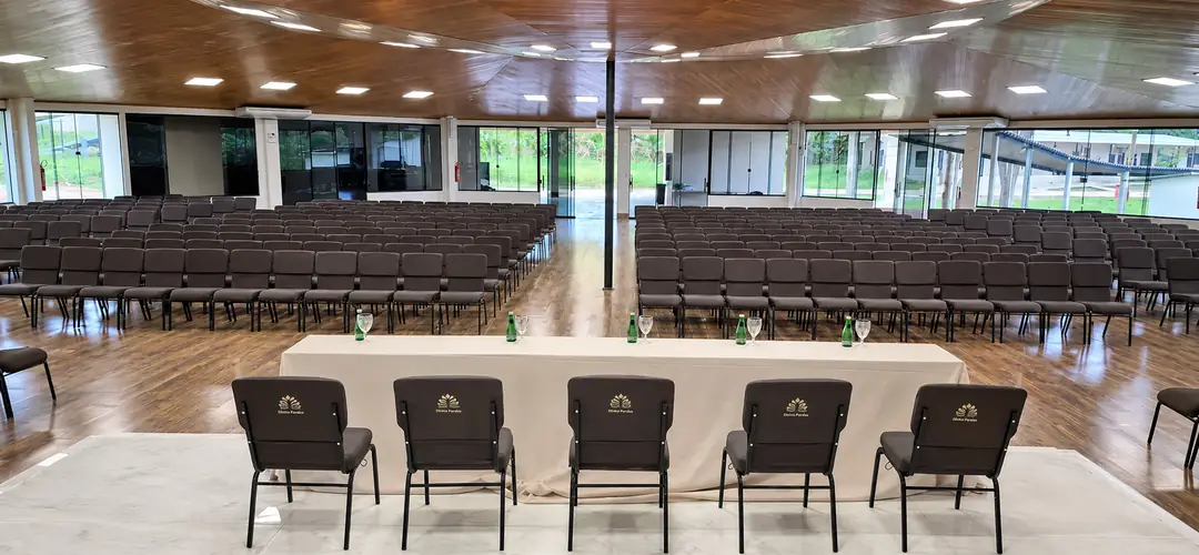 Auditório Tuiuiú com mesa diretora, microfones e fileiras de poltronas, e paredes de vidro para o verde